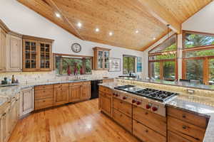 Kitchen with decorative light fixtures, glass insert cabinets, light stone counters, stainless steel gas stovetop, and high vaulted ceiling