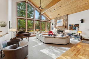 Living area featuring high vaulted ceiling, a stone fireplace, plenty of natural light, wood finished floors, and wooden ceiling