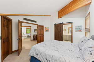 Bedroom with light carpet, a barn door, and ensuite bath