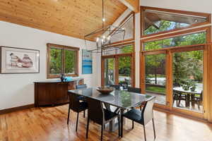 Dining space with light wood-style floors, a chandelier, high vaulted ceiling, and a wooden ceiling with exposed beams