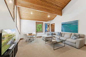 Living room with a wooden ceiling with exposed beams, light carpet, and high vaulted ceiling