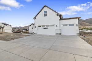 View of side of home with a mountain view, concrete driveway, a garage, and stone siding