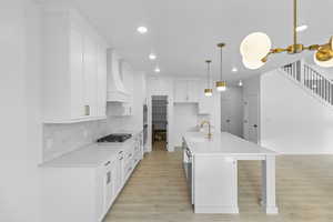 Kitchen featuring white cabinets, light wood finished floors, light stone counters, decorative backsplash, large pantry, and recessed lighting