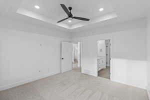 Primary Bedroom with a tray ceiling, light carpet, a ceiling fan, connected bathroom, and recessed lighting