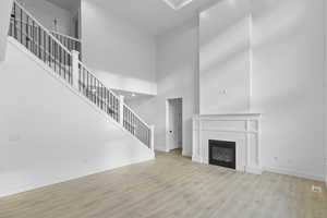Living room featuring stairs, a high ceiling, light wood-type flooring, and a tile fireplace