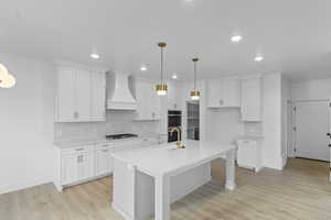Kitchen with decorative backsplash, hanging light fixtures, a kitchen bar, white cabinetry, and custom range hood