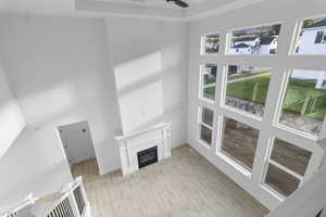 Looking down on living room with a glass covered fireplace, light wood finished floors, a high ceiling, ceiling fan, and a 2-story wall of windows