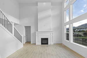 Living room featuring a high ceiling, light wood-type flooring, a fireplace, stairs, and a mountain view