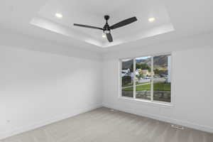 Primary Bedroom with light carpet, a raised ceiling, recessed lighting, and ceiling fan