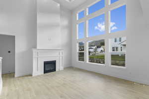 Living room featuring a towering ceiling, a glass covered fireplace, and light wood-type flooring