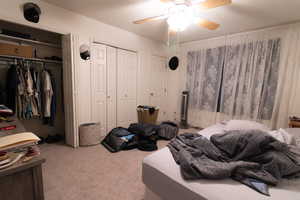 Bedroom featuring light carpet, multiple closets, and ceiling fan