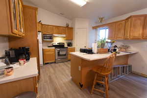 Kitchen featuring light countertops, appliances with stainless steel finishes, light wood-style flooring, a breakfast bar, and vaulted ceiling