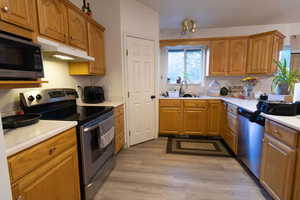 Kitchen with stainless steel appliances, light countertops, brown cabinetry, and under cabinet range hood