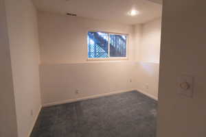 Unfurnished room featuring dark colored carpet and baseboards