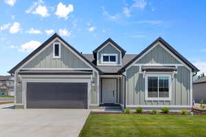 View of front of home featuring roof with shingles, concrete driveway, board and batten siding, and a front yard