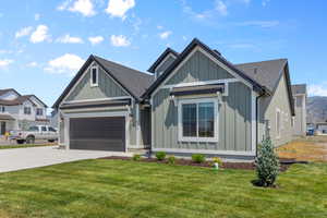 View of front of home featuring board and batten siding, concrete driveway, roof with shingles, and a front yard