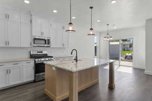 Kitchen featuring stainless steel appliances, light stone counters, white cabinetry, an island with sink, and decorative backsplash