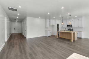 Kitchen featuring white cabinetry, an island with sink, recessed lighting, open floor plan, and dark wood-type flooring
