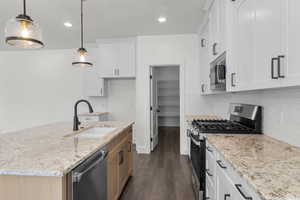 Kitchen with appliances with stainless steel finishes, a center island with sink, light stone countertops, white cabinets, and dark wood-type flooring