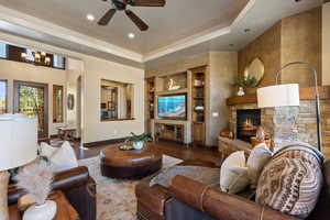 Living room with a tray ceiling, built in shelves, a fireplace, recessed lighting, and wood finished floors