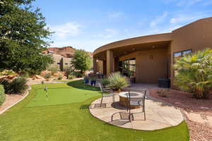 Back of house featuring a patio area, stucco siding, a putting area, and a fire pit