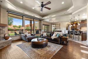 Living room featuring a raised ceiling, a chandelier, a ceiling fan, dark wood-style floors, and arched walkways