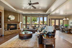 Living room featuring a raised ceiling, a stone fireplace, dark wood-style flooring, and recessed lighting