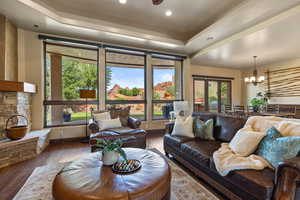 Living area with a tray ceiling, hardwood / wood-style flooring, a chandelier, recessed lighting, and a stone fireplace