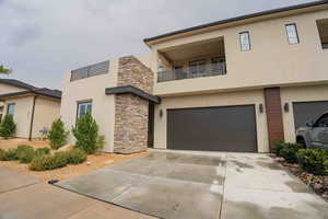 Modern home with stucco siding, a balcony, concrete driveway, and stone siding