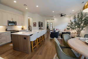 Kitchen featuring a center island with sink, stainless steel microwave, decorative backsplash, gas stove, and recessed lighting