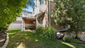 Back of house featuring brick siding, a patio, a lawn, and a new Trex deck. Low maintenance yard with fully wooded sloped backyard for privacy, nature and beauty.