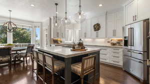 Brand new Kitchen featuring white cabinetry, backsplash, top of the line appliances, motion faucet, built-in cup washer, corner window, hanging light fixtures, high end refrigerator, and recessed lighting