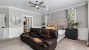 Extra Large Owner's Suite Bedroom featuring a wainscoted wall, a decorative wall, crown molding, carpet, in-wall safe and ceiling fan