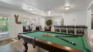 Playroom featuring wood finished floors and billiards- next to bar stool area and wet bar.