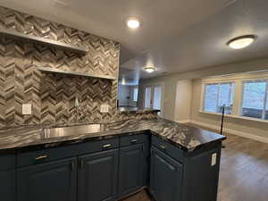Kitchen with dark wood finished floors, dark stone counters, backsplash, a peninsula, and a textured ceiling