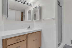 Bathroom featuring tile walls, vanity, a shower stall, and a wainscoted wall