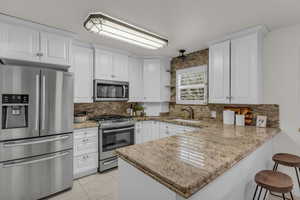 Kitchen featuring appliances with stainless steel finishes, tasteful backsplash, white cabinets, a peninsula, and a breakfast bar