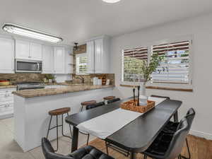 Kitchen featuring decorative backsplash, light stone counters, and white cabinetry