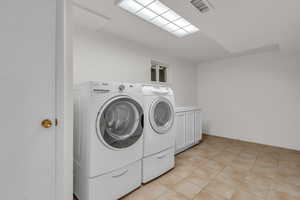Laundry area featuring washing machine and clothes dryer, cabinet space, and light tile patterned flooring