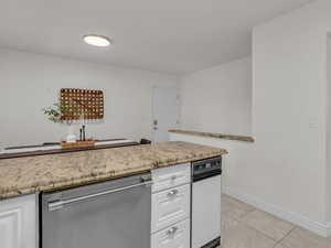 Kitchen with stainless steel dishwasher, white cabinets, light tile patterned floors, and light stone countertops