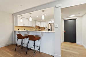 Kitchen featuring white cabinets, light wood-style floors, a kitchen bar, decorative light fixtures, and stainless steel fridge