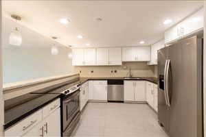 Kitchen with appliances with stainless steel finishes, decorative light fixtures, light tile patterned flooring, recessed lighting, and white cabinets