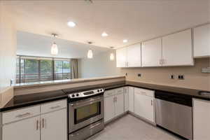 Kitchen featuring appliances with stainless steel finishes, white cabinets, light tile patterned floors, hanging light fixtures, and a peninsula