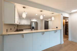 Kitchen with a kitchen breakfast bar, light stone counters, stainless steel refrigerator with ice dispenser, recessed lighting, and light wood finished floors