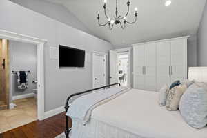 Bedroom featuring dark wood-style flooring, a closet, lofted ceiling, a chandelier, and connected bathroom