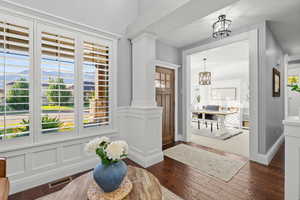 Foyer featuring dark wood-type flooring, ornate columns, a decorative wall, a wainscoted wall, and a chandelier