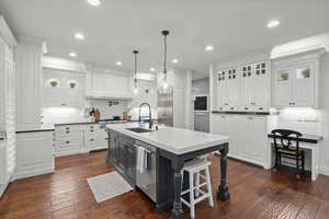 Kitchen with glass insert cabinets, a center island with sink, a breakfast bar, dark wood-style floors, and recessed lighting