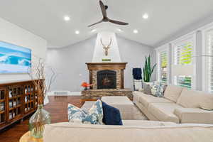 Living area with dark wood-style flooring, vaulted ceiling, a stone fireplace, ceiling fan, and recessed lighting