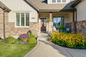Doorway to property featuring stone siding, roof with shingles, board and batten siding, and covered porch