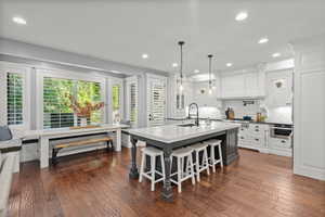 Kitchen with hanging light fixtures, dark wood finished floors, white cabinets, backsplash, and recessed lighting